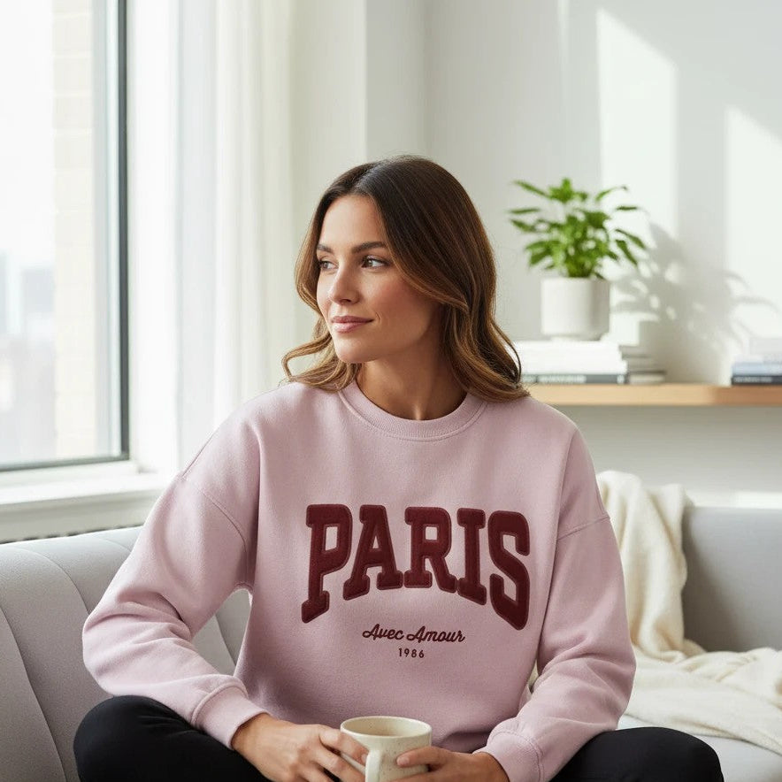 Antique Rose Boutique chalk pink long sleeve sweatshirt with PARIS embroidery worn by a woman sitting on a sofa