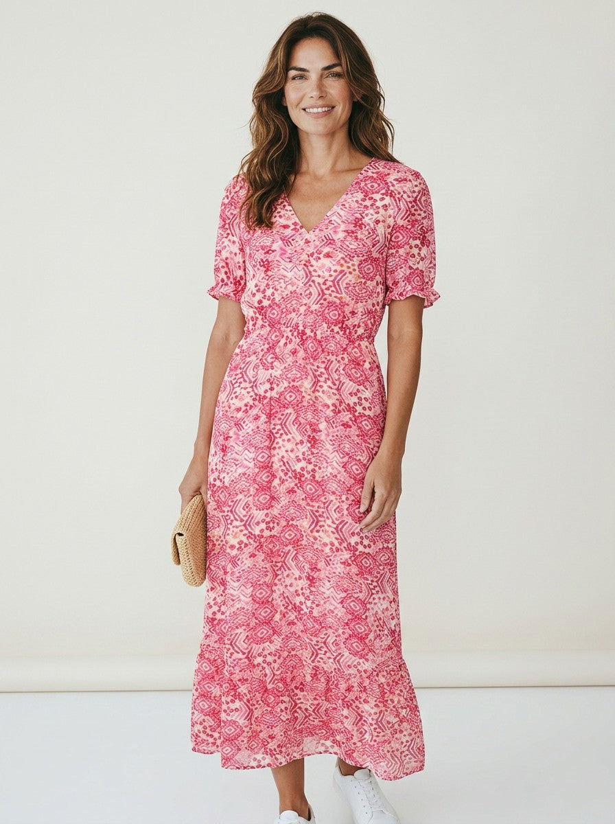 Antique Rose Boutique coral pink long V-neck dress with short sleeves and Aztec print, worn by a smiling woman.