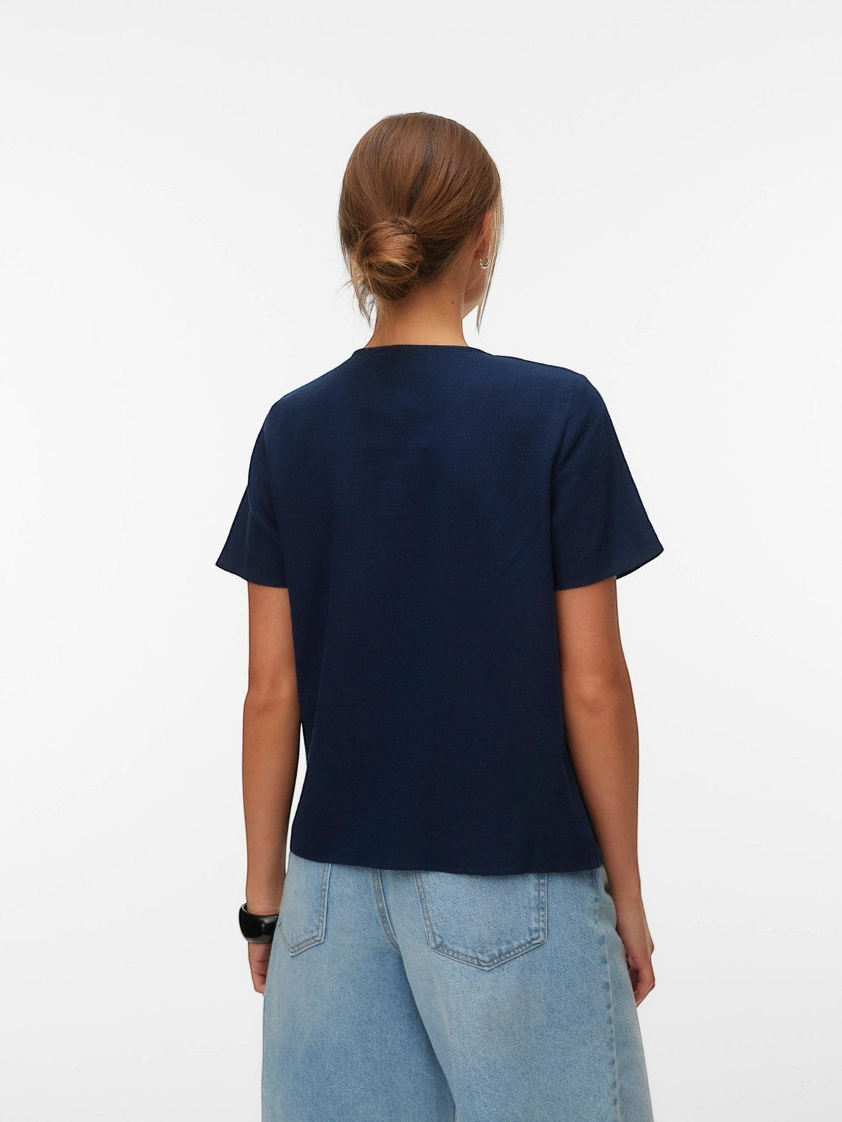 Antique Rose Boutique navy blue linen-mix V-neck top worn by a model from the back view with light wash denim jeans