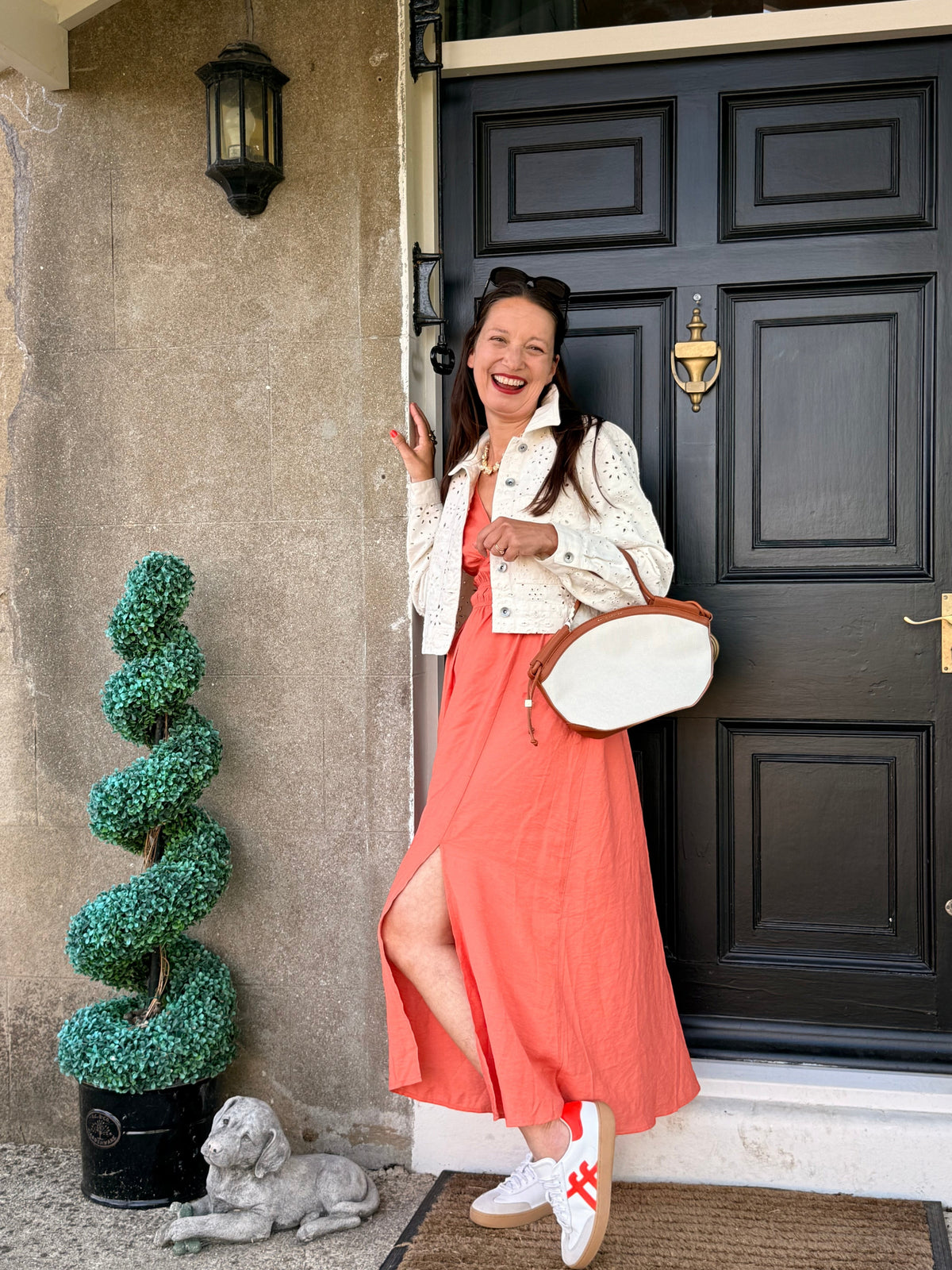 Antique Rose Boutique model wearing a langoustino orange Vero Moda midi dress with a side slit and white jacket