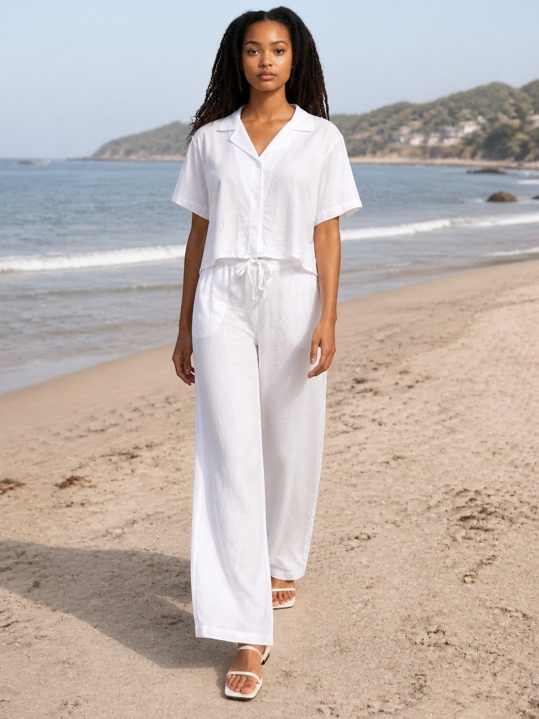 Antique Rose Boutique white linen wide-leg trousers and matching button-down shirt worn by a model on a sandy beach