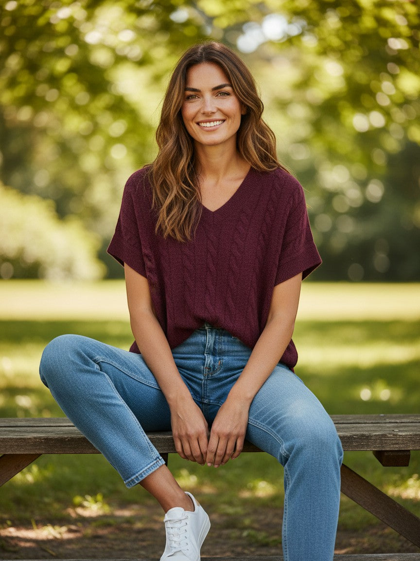 Antique Rose Boutique fig wine red cable knit short sleeve V-neck vest worn by a smiling woman on a park bench.